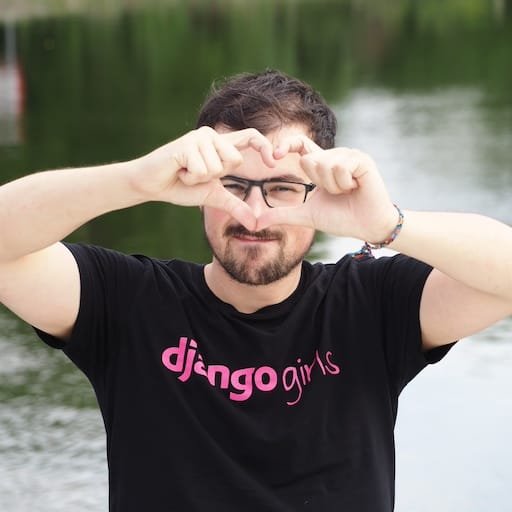 Thibaud Colas wearing a black shirt that says django girls in pink, he is making a heart with his hands